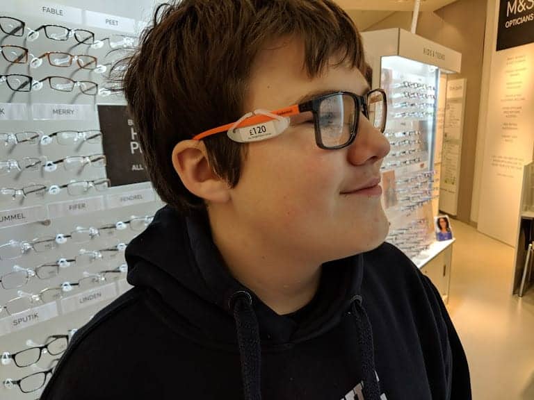 A teenage boy tries on some glasses with black plastic frame