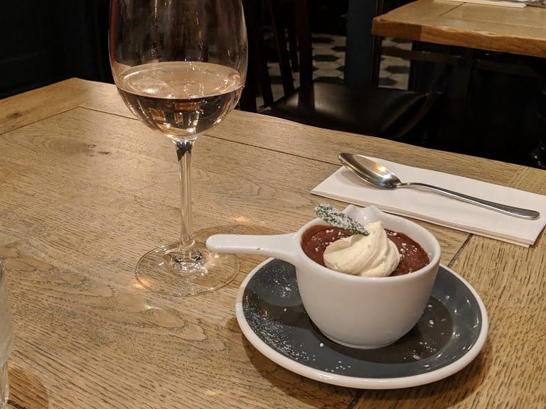 Dark chocolate mousse topped with cream and sprinkled with icing sugar, with a glass of wine