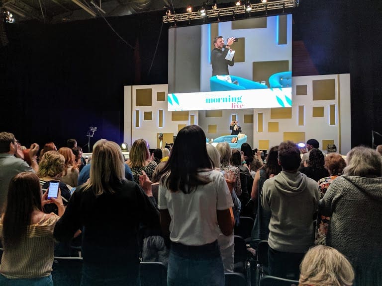 Warm up act on stage with rows of people standing watching taking photos