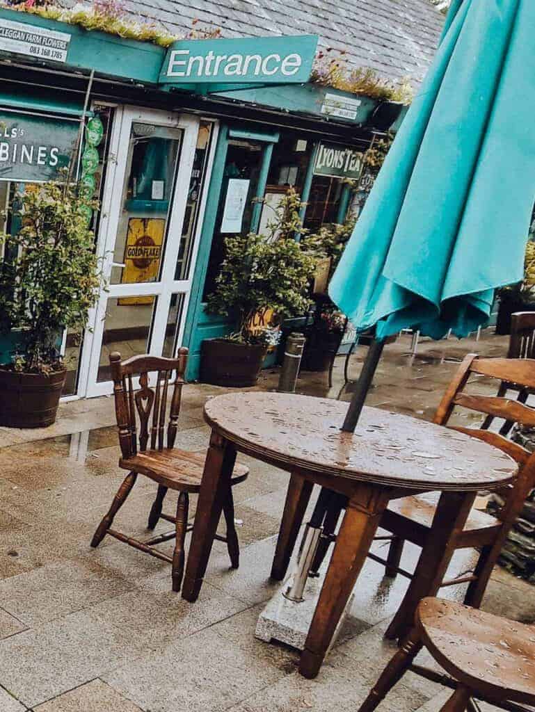 A rainy day at the entrance of Veldons Seafarer Bar & Restaurant, showing wet wooden tables and chairs outside, with the restaurant's green sign and entrance door in the background.