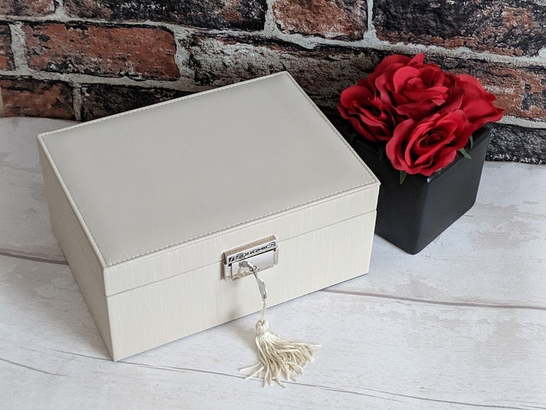 A key with a tassle inside the lock of a white jewellery box