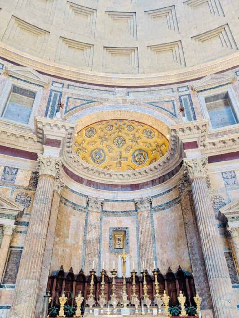 Ornate golden altar inside the Pantheon in Rome, featuring tall marble columns, detailed mosaics, and symmetrical religious decorations beneath the coffered dome.