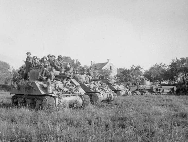 Sherman-tanks met Britse infanterie wachten op bevel om op te rukken bij de start van Operatie Goodwood tijdens de Slag om Caen.