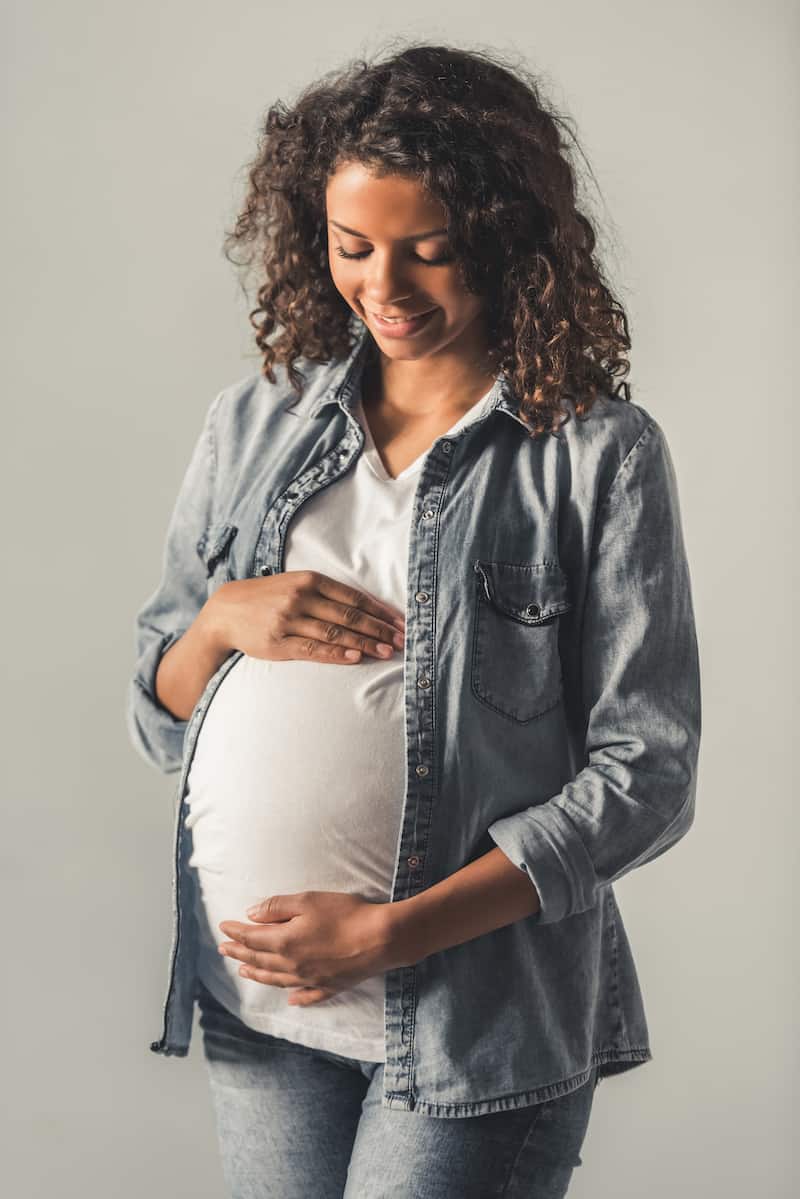 Pregnant Afro American woman is touching her tummy.