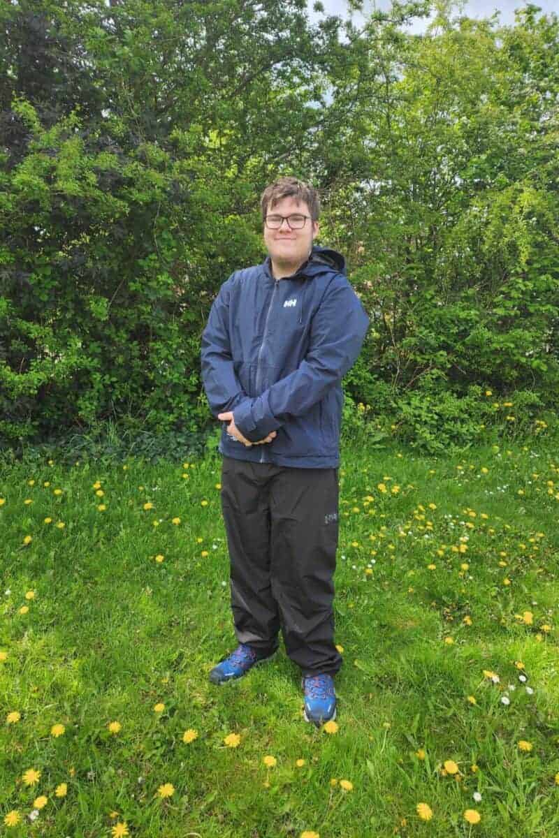 Teenage boy standing in hiking gear on grass.