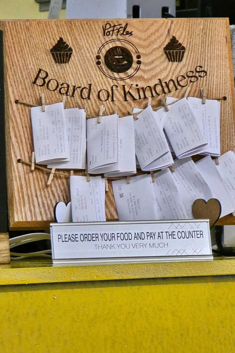 At PoFfles Coffee and Cake Emporium in Mansfield, a wooden "Board of Kindness" features pinned receipts. Below, a sign kindly asks, "Please order your food and pay at the counter. Thank you very much." A delightful spot in town that deserves a great review!.