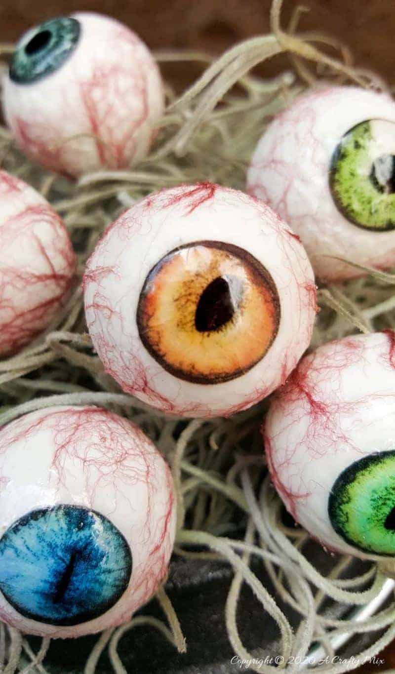 Up the creepy stakes this Halloween and make these realistic eyeballs for Halloween. Quick and budget-friendly they'll add just the right spooky factor to your decor. The tutorial includes free "iris" printables to use #HalloweenDecor #CreepyEyeballs #ACraftyMix #FreePrintables