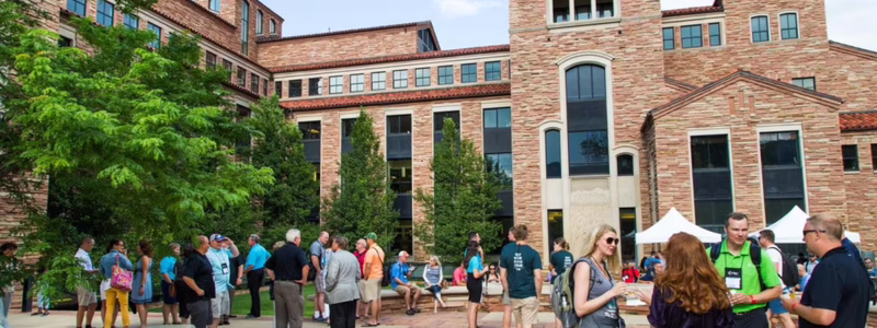 Crowd of attendees engaging outside a university building at CU Boulder, showcasing a vibrant conference atmosphere.
