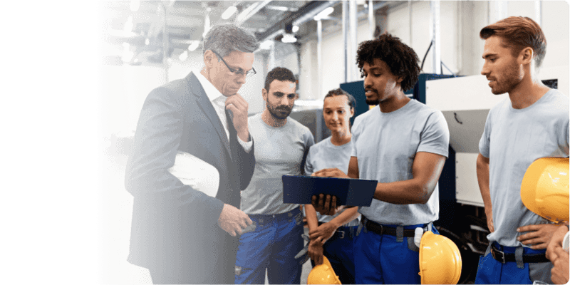 Executive talking with construction workers who are showing him a tablet.