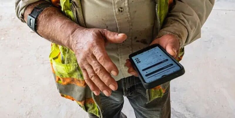 Construction worker looking at VigiLife app on smartphone.