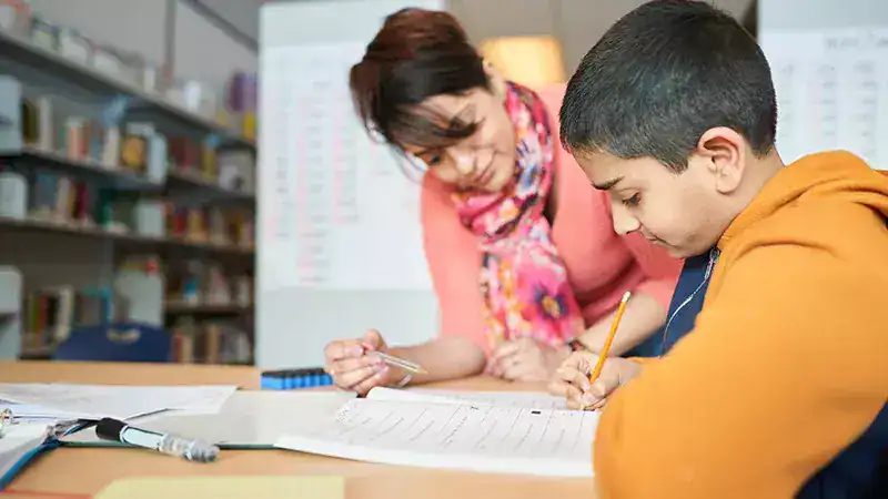 Enseignante accompagnant un jeune élève dans un exercice d'écriture en classe.