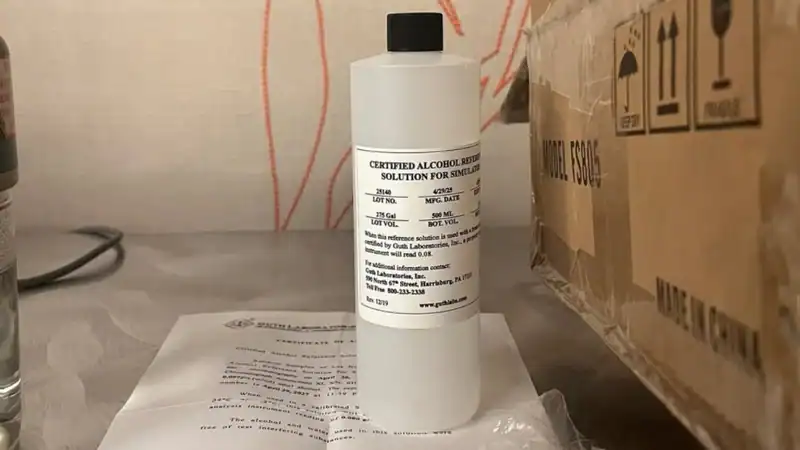 A white plastic bottle labeled "Certified Alcohol Reference Solution for Simulator" by Guth Laboratories, sitting on a table next to a certification document.