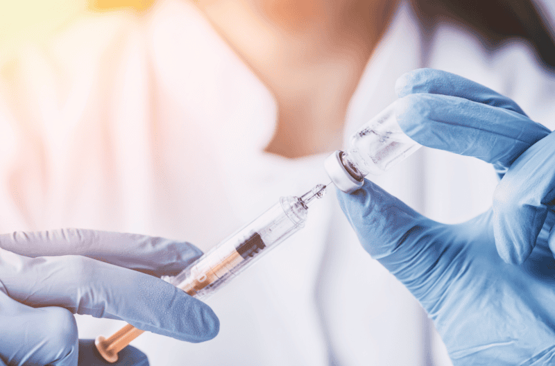 Pharmacists holding a vaccine vial and needle with gloves.
