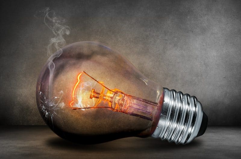 bombilla encendida apoyada sobre el suelo en posición horizontal, con el cristal roto y humo saliendo de la abertura