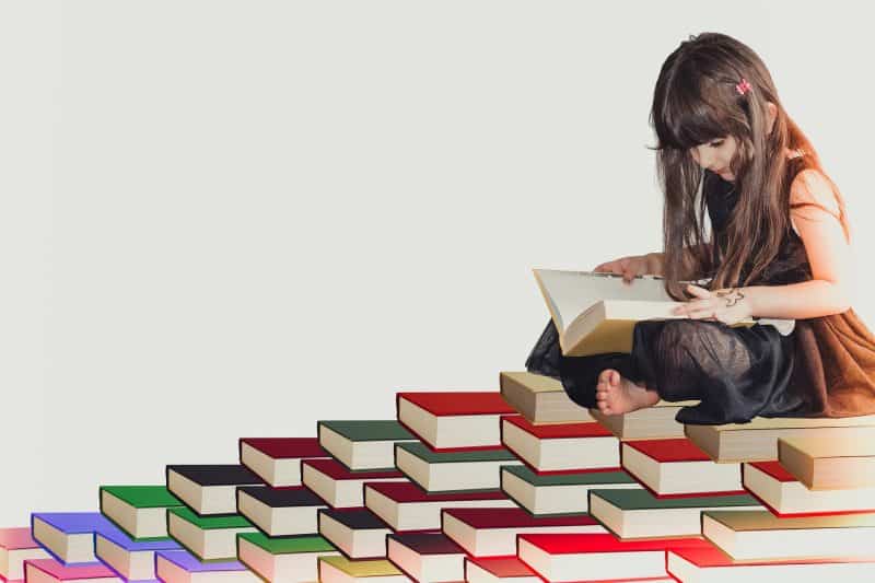 Niña leyendo, sentada sobre una montaña de libros