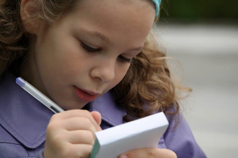 Niña escribiendo con bolígrafo en bloc de notas