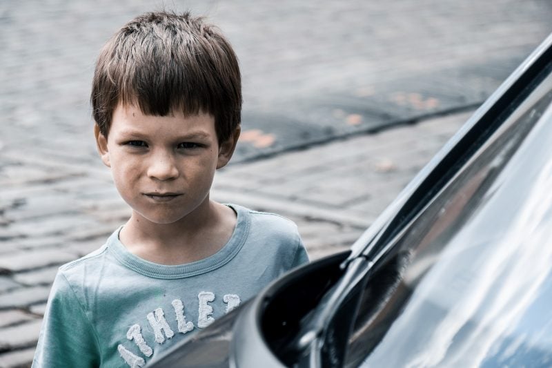 Niño con cara de enfado junto a vehículo