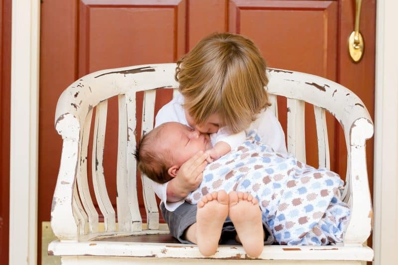 Niño pequeño sentado sobre una silla sujeta a un bebé y le besa la cabeza