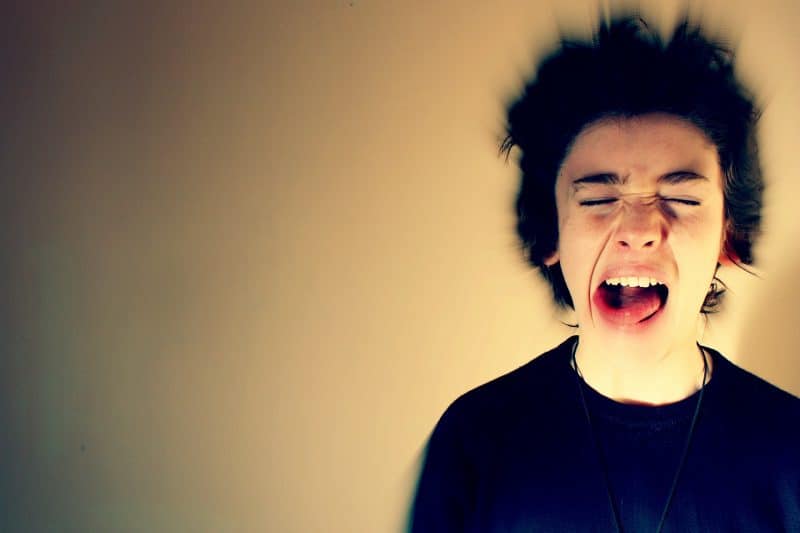 Adolescente con la cara en posición de gritar, con los ojos cerrados, la boca abierta, la lengua fuera y el pelo difuminado