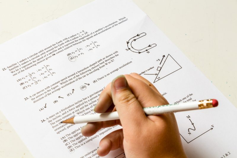 Mano infantil agarrando lapicero blanco, sobre un examen de matemáticas en inglés
