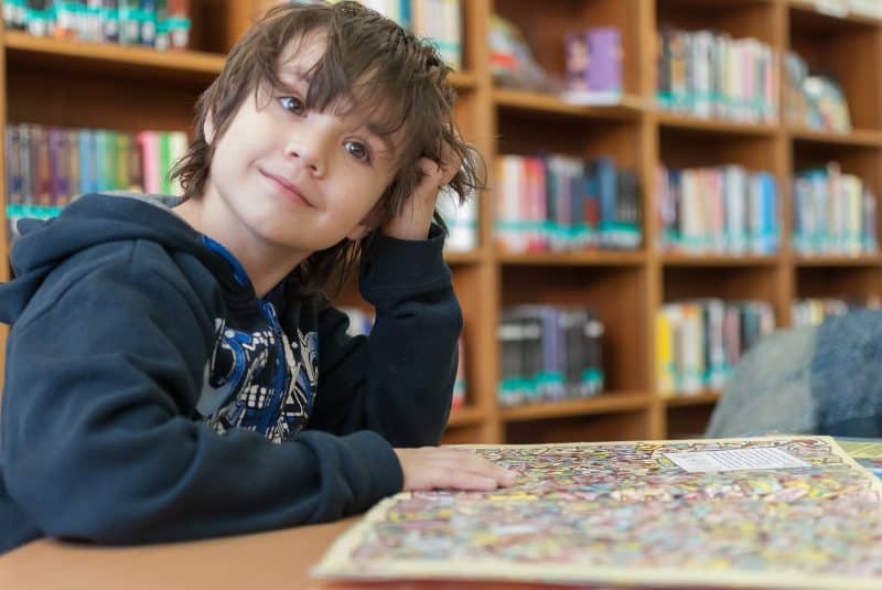 Niño sosteniendo un libro con dibujos en la mesa de una biblioteca.