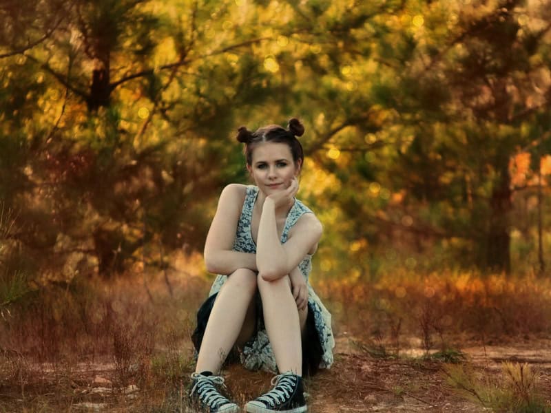 Adolescente con vestido y moños, sentada en el bosque