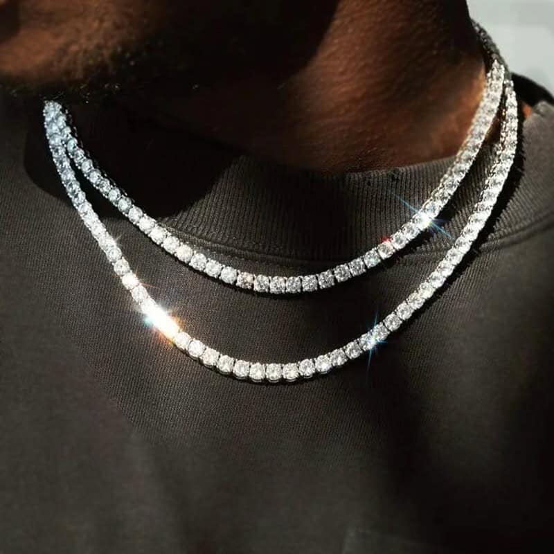 A close-up of a person wearing two sparkling diamond tennis chains, a stunning example of men's jewellery, layered over a black shirt. The necklaces catch the light, highlighting the brilliance of the stones against the dark fabric.