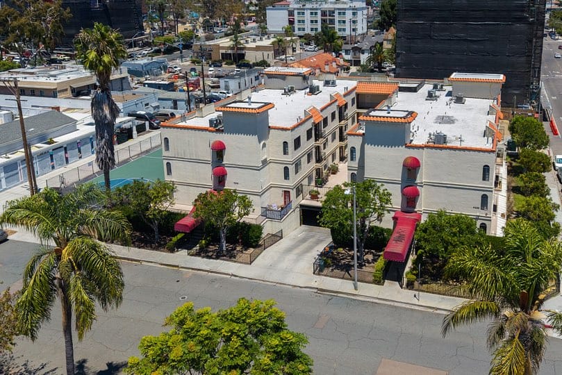 Elevated view of a multi-story stucco condominium complex with central driveways, red awnings, palm trees, and an adjacent sports court at 205 Ohio St Unit 304 in North Park.