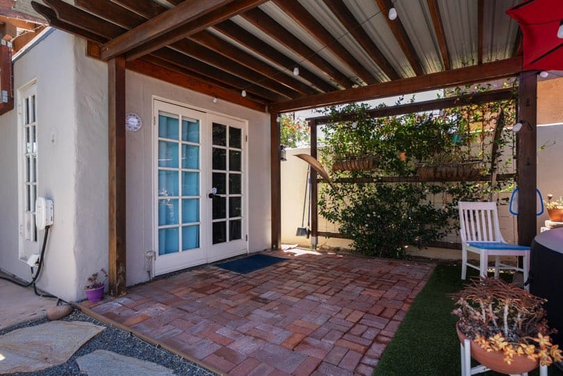 Covered brick patio area with a wooden pergola, string lights, white French doors, EV charger, and trellis greenery at 3381 Bancroft St in North Park