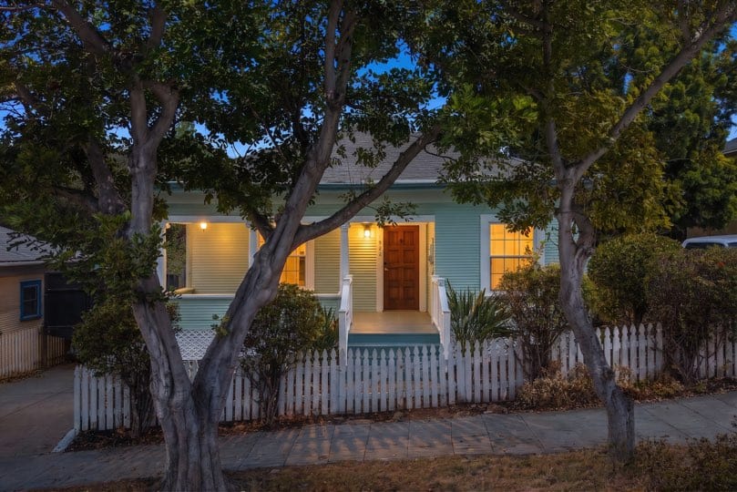 A light green single-story house with a covered porch sits behind a white picket fence at 1932 C Street in Golden Hill.