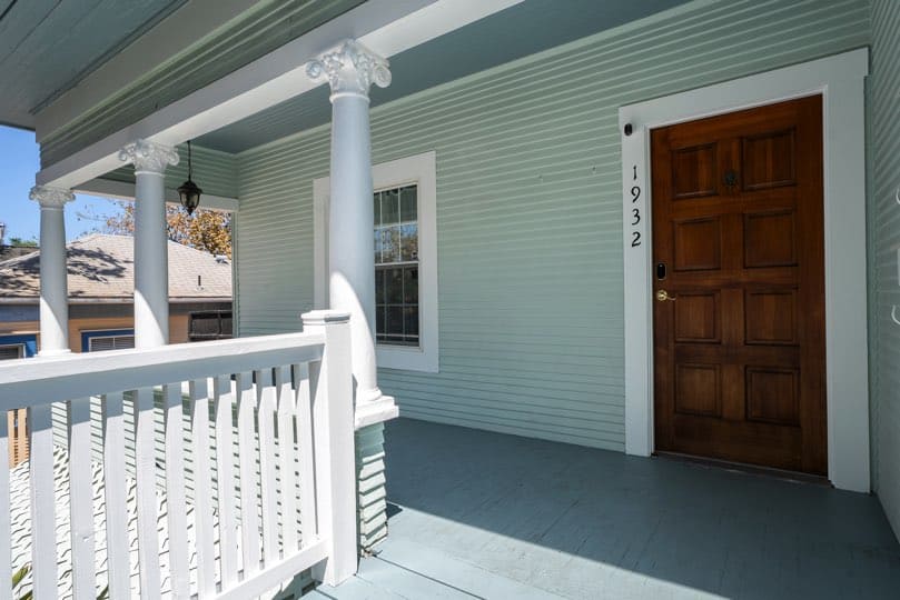 A dark wood paneled front door with white trim and house numbers 1932 is set on a covered front porch with white columns at 1932 C Street in Golden Hill.