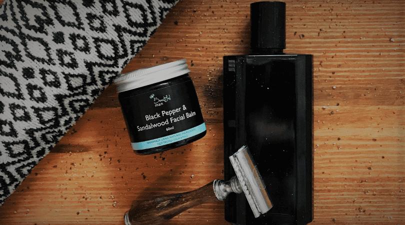 beeutiful facial balm for men, a towel, a razor and aftershave laying on a wooden plank