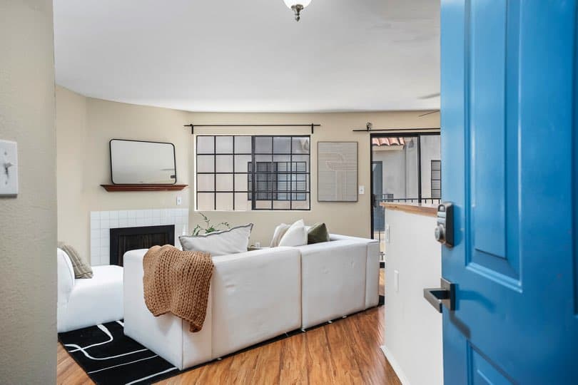 Living room viewed from an open blue front door, featuring hardwood floors, a white sectional sofa, a tiled fireplace, a grid window, and a sliding glass door at 205 Ohio St Unit 304 in North Park.