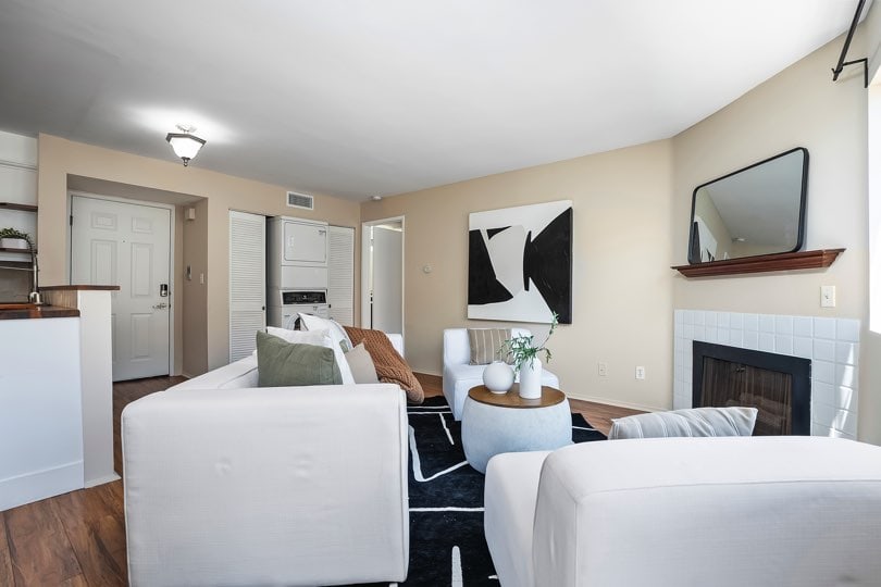 Living room with white sofas, a tiled fireplace with a mantel and mirror, a black and white geometric rug, and a stacked washer and dryer in the background at 205 Ohio St Unit 304 in North Park.