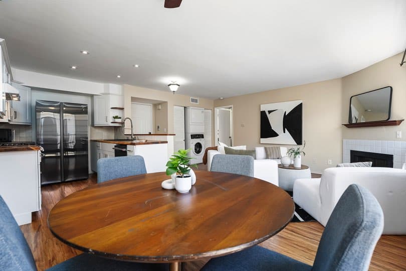 Dining area with a round wooden table and blue chairs looking out toward an open-concept living room and kitchen space at 205 Ohio St Unit 304 in North Park.