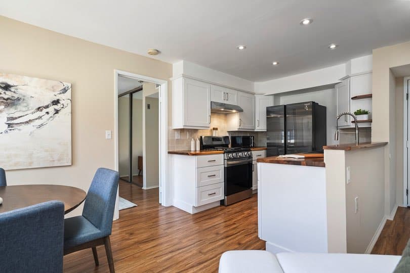 Kitchen featuring white cabinetry and wood countertops next to a dining area with blue upholstered chairs and an open doorway leading to a bedroom at 205 Ohio St Unit 304 in North Park.