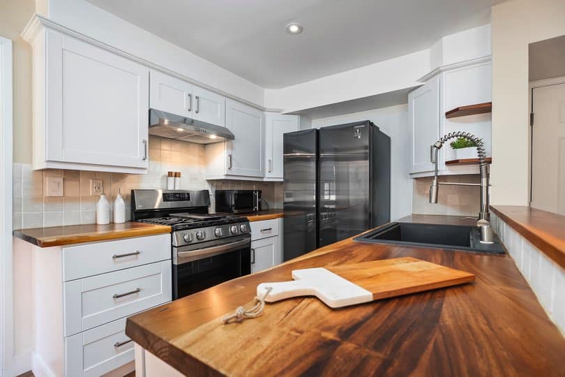 Kitchen featuring wood countertops, white cabinetry, stainless steel and black appliances, a sink with a spring-neck faucet, and a cutting board on the foreground island counter at 205 Ohio St Unit 304 in North Park.