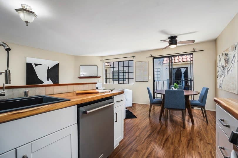 Kitchen foreground with wood countertops and a stainless steel dishwasher looking out toward a dining area with a round table and blue chairs at 205 Ohio St Unit 304 in North Park.