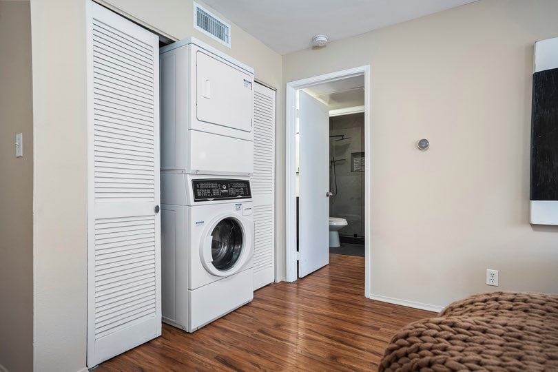 Stacked white washer and dryer unit inside a closet with white louvered doors, situated on wood-look flooring next to an open doorway leading to a bathroom at 205 Ohio St Unit 304 in North Park.