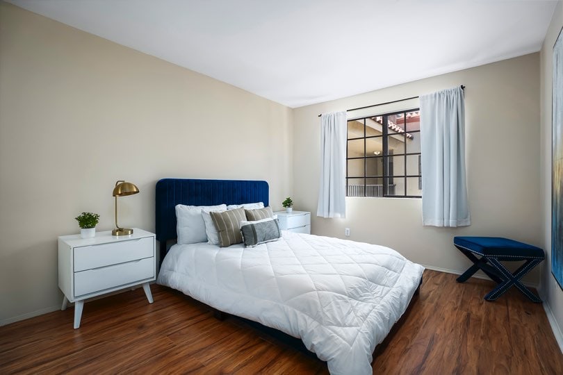 Bedroom with a blue velvet headboard, white nightstands, wood-look floors, a small blue bench, and a grid-style window at 205 Ohio St Unit 304 in North Park.