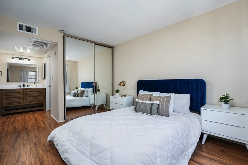 Bedroom featuring a blue velvet headboard, white nightstands, wood-look floors, a large sliding mirrored closet door, and an attached bathroom vanity at 205 Ohio St Unit 304 in North Park.