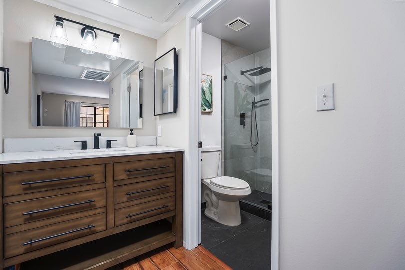 Bathroom with a dark wooden vanity, large mirror with glass light fixtures, and an open doorway showing a white toilet and a glass-enclosed shower at 205 Ohio St Unit 304 in North Park.