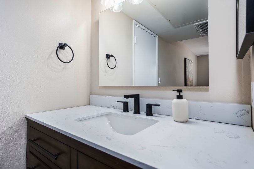 Bathroom vanity featuring a white marbled countertop, undermount sink, dark modern fixtures, a large mirror, and a dark wood cabinet at 205 Ohio St Unit 304 in North Park.