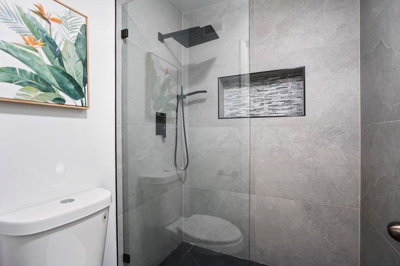 Bathroom featuring a white toilet next to a glass-enclosed shower with large gray wall tiles, dark fixtures, and a mosaic-tiled shelf niche at 205 Ohio St Unit 304 in North Park.