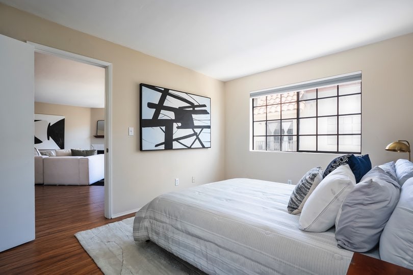 Bedroom with a grid-style window, wood-look floors, a large black-and-white abstract painting, and an open doorway looking into a living room area at 205 Ohio St Unit 304 in North Park.