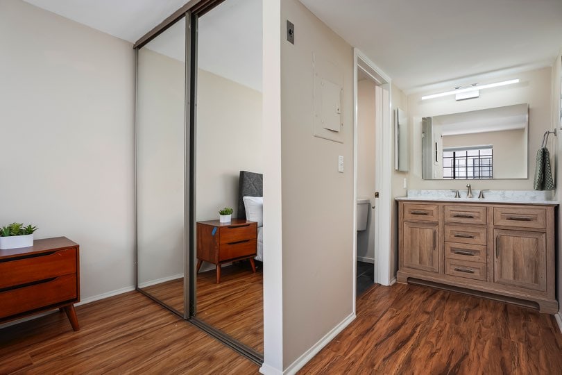Bedroom area featuring wood-look floors, a sliding mirrored closet door, and an open bathroom vanity with a wooden cabinet and mirror at 205 Ohio St Unit 304 in North Park.