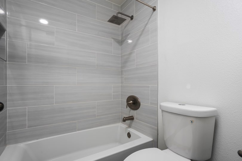 Bathroom featuring a white toilet next to a bathtub and shower surround with light gray horizontal tiling and dark metallic fixtures at 205 Ohio St Unit 304 in North Park.