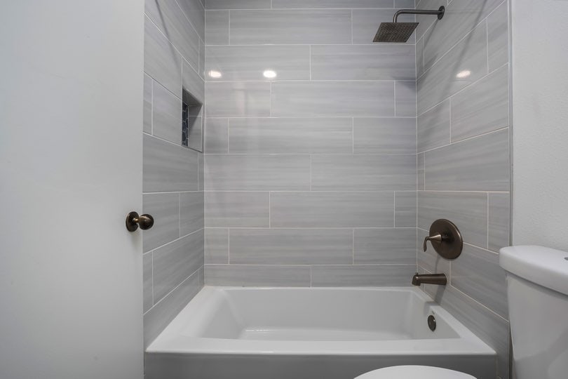 White bathtub and shower with light gray horizontal wall tiles, dark metallic fixtures, and a built-in shelf niche at 205 Ohio St Unit 304 in North Park.