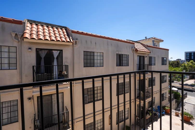 View from a private balcony with black metal railings looking across toward multi-story stucco building units with window grids and red clay roof tiles at 205 Ohio St Unit 304 in North Park.