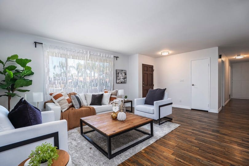 Living room with dark wood floors, white walls, and a wood coffee table surrounded by white seating at 5237 Diane Ave in Clairemont.